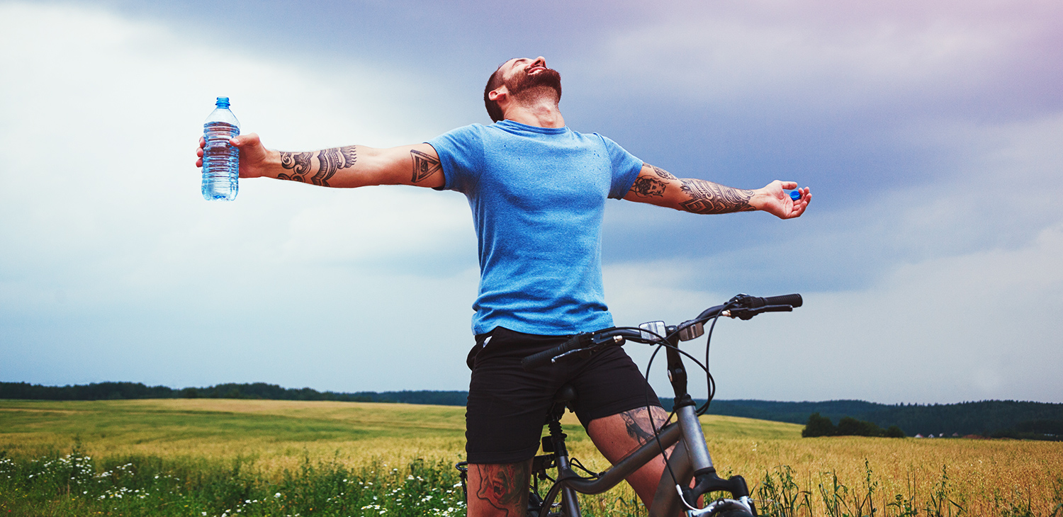 Uomo felice con la bici che allarga le mani e beve acqua riposando.